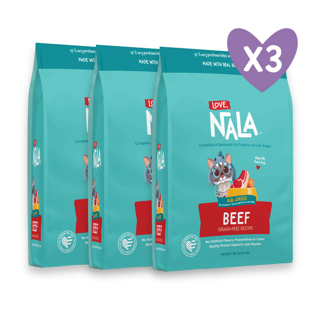 Three bags of NALA Love Beef Grain-Free Cat Food are shown in a clean studio-style arrangement with a purple heart-shaped 'x3' overlay on the top right. The bags are teal with red and white branding, and the front bag features a cat illustration and a beef graphic.